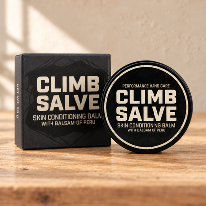 Climb Salve 25g tin and retail box on a warm wooden surface