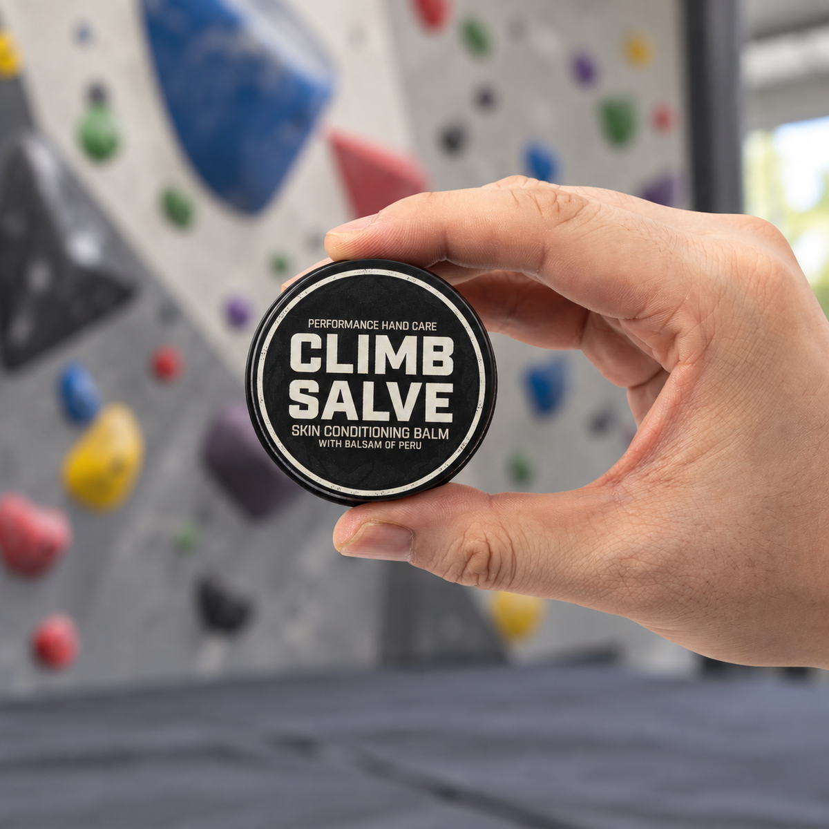Climb Salve 25g tin held up in an indoor climbing gym