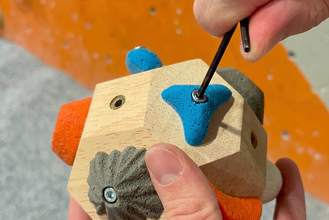 Hands attaching a brightly colored climbing hold to the Boulder Block with a hex key