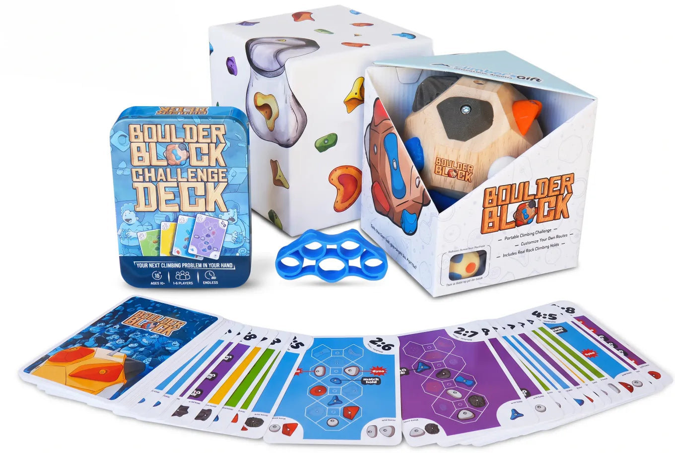 Flat-lay of the Boulder Block box contents: the wooden block with climbing holds, the blue Challenge Deck tin, a finger exerciser, and a fanned deck of route cards