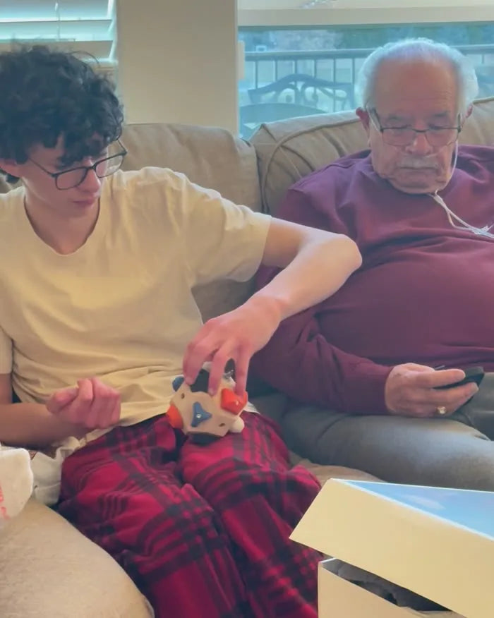 A teenager working the Boulder Block on the sofa next to his grandfather, who is on his phone