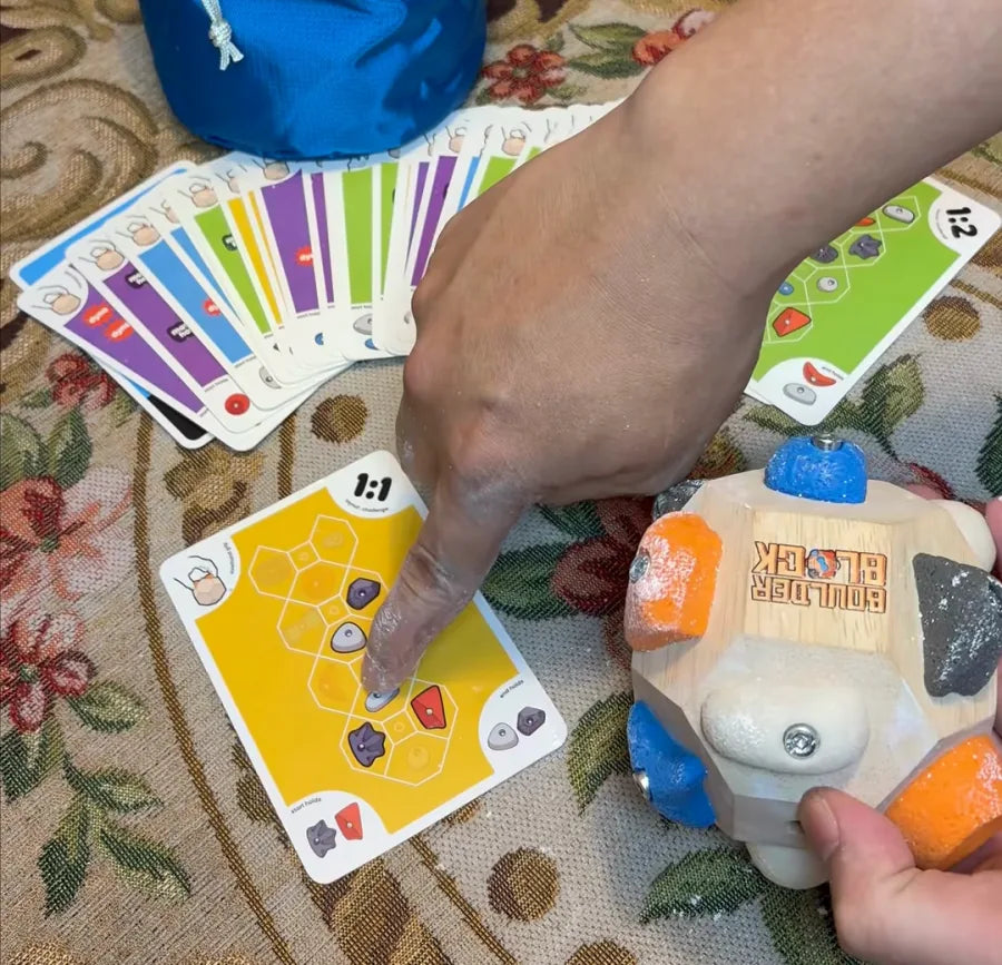 A finger tracing the route on a yellow Challenge Deck card, the Boulder Block and the fanned-out deck beside it